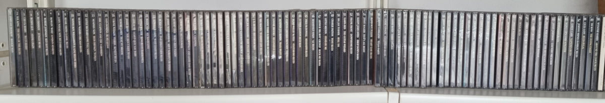 A long row of black plastic DVD or VHS cases standing upright on a shelf, photographed against a light wall.