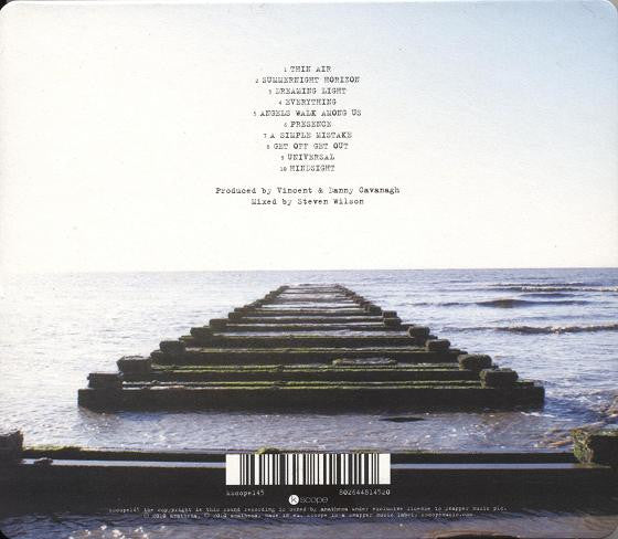The back cover of a music album featuring a photograph of a concrete pier extending into calm water under a pale sky, with track listing text and a barcode printed on it.