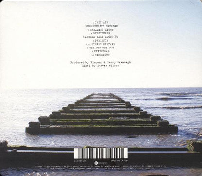 The back cover of a music album featuring a photograph of a concrete pier extending into calm water under a pale sky, with track listing text and a barcode printed on it.