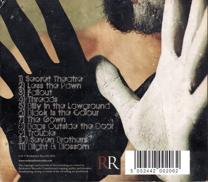 Back cover of a music album featuring a close-up of a person's face with black and white painted hands, a track list on the left, and a barcode at the bottom right.