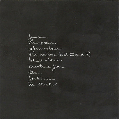 A black square card or print featuring white handwritten text listing song titles and names, including 'Home', 'Thump sin', 'Skinny love', 'The wolves (Act I and II)', 'Blindside', 'Creature fear', 'For Emma', and 'Le: Attack'.