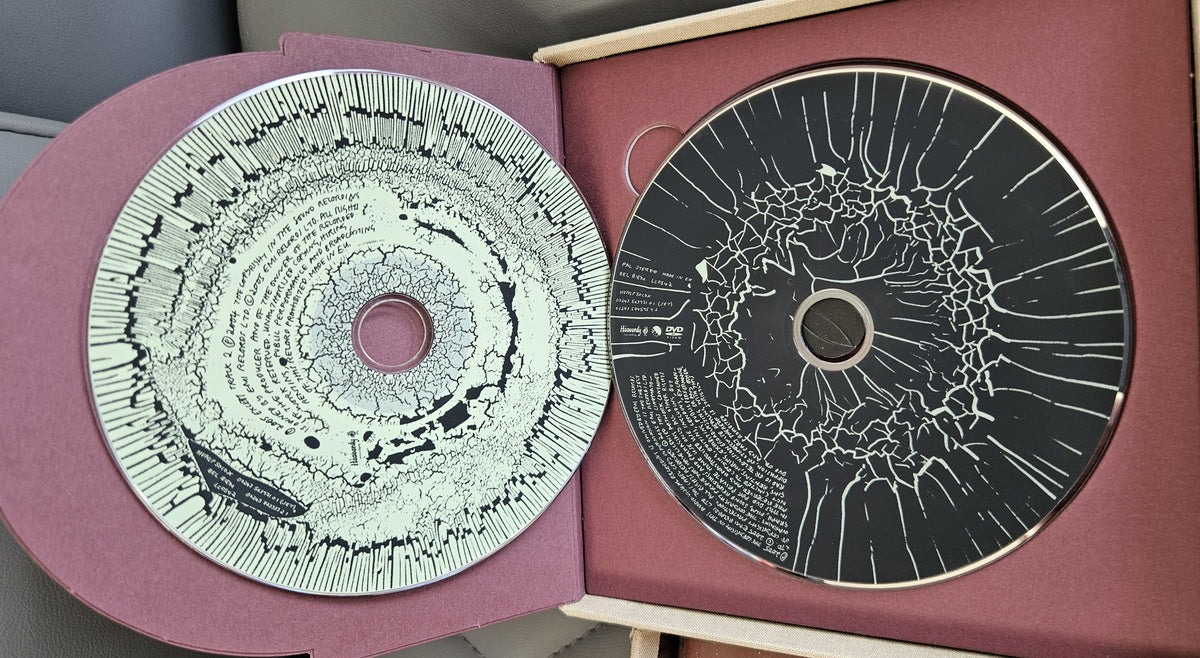 An open presentation box containing two circular art discs with intricate black and white abstract line patterns on a burgundy background.