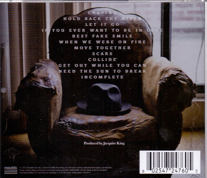 Back cover of a music CD for the band Cradle Of Filth, featuring a dark, moody photograph of a worn armchair with a black hat resting on it, and a list of track titles printed in white text.