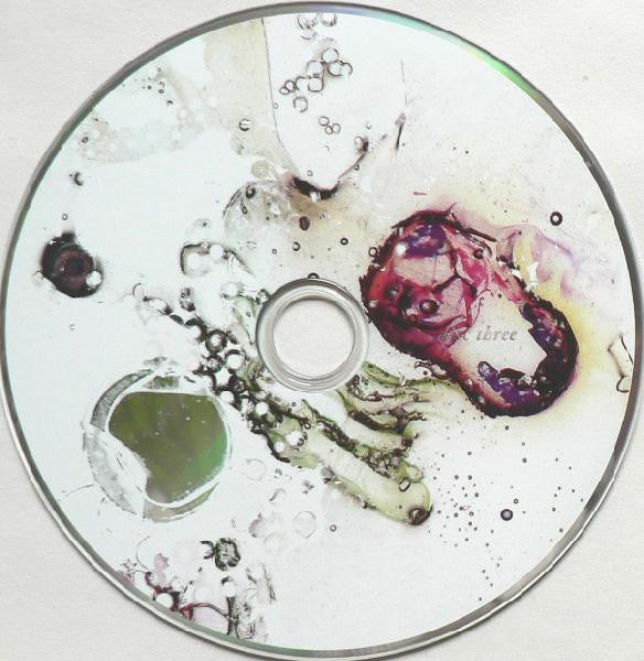 A circular disc with an abstract printed design featuring splashes of purple, green, black, and yellow on a white background, photographed from above.