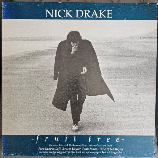 The front cover of the Nick Drake 'Fruit Tree' vinyl record compilation, featuring a black and white photograph of the artist walking on a beach with blue bands at the top and bottom.