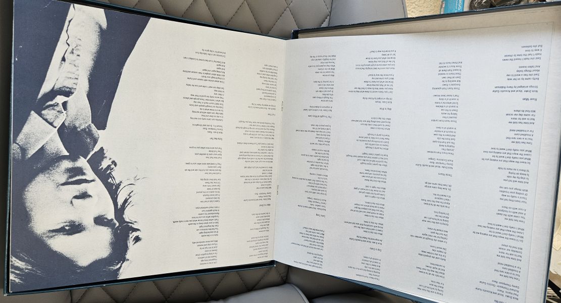 An open book or album booklet laid flat, showing printed text columns on the left page and a black-and-white portrait of a person on the right page.