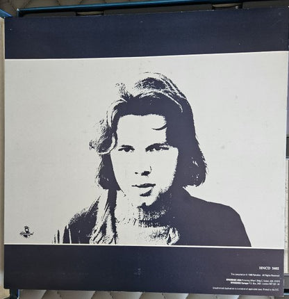 A square black-and-white printed artwork or poster featuring a stylized portrait of a person, photographed against a dark navy background. The print has a white central panel with a black-and-white face illustration and dark navy bands at the top and bottom, including small text in the lower right.