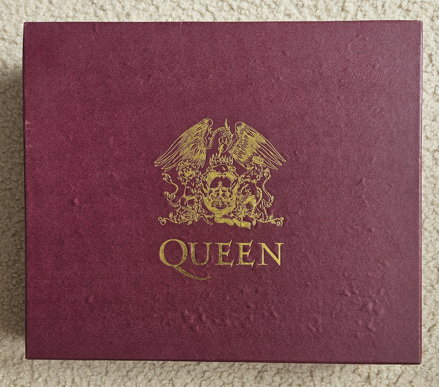 Maroon album cover with gold emblem and 'Queen' text on a textured surface