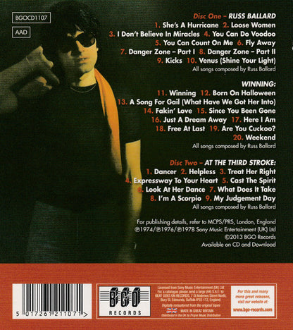 Back cover of a music CD for Russ Ballard's 'Winning' album, showing track listings, barcode, and release details on a dark background with a red band at the bottom.