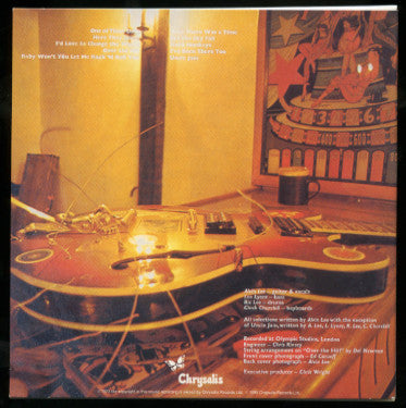 The back cover of a Chrysalis CD album, featuring a warm-toned photograph of a guitar on a table with a mug and framed art in the background. Tracklist and credits are printed in white text.