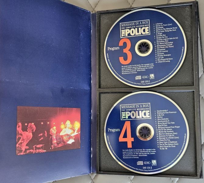 The Police 'Message in a Box' live performances CD set, showing Program 3 and 4 on blue discs inside a black case next to the blue slipcover with a printed concert photo.