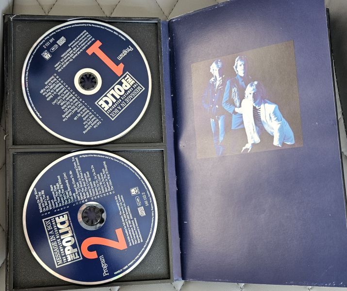 A used CD case for the band 'The Police' 'Police' album, showing two CD-ROMs in the black foam insert and the open blue jewel case cover with a photo of the band members.