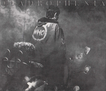 Black and white album cover art for 'Quadrophenia' featuring a person from behind wearing a jacket with a large 'WHO' logo on the back, seated in a car with mirrors and smoke visible.