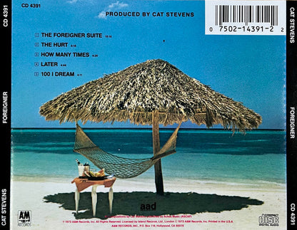 Back cover of the CD release for Cat Stevens' album 'Foreigner', featuring a beach scene with a thatched umbrella, hammock, and blue ocean under a bright blue sky. Tracklist, barcode, and artist/label text are visible.